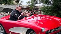 Ein kleines Mädchen sitzt mit ihrem Vater in einem roten Modellauto als Cabrio. 