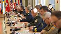 Soldaten mehrerer Nationen sitzen an einem langen Tisch
