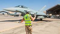 Ein Soldat in Warnweste steht vor dem Eurofighter und gibt dem Piloten Handzeichen damit er den Schelterbereich verlassen kann.