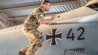 Ein Soldat steht auf einem Eurofighter und schaut mit einer Taschenlampe nach Beschädigungen.
