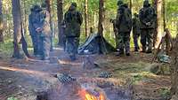 Mehrere Personen im Feld vor Zelten, vorne brennt ein Lagerfeuer