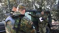Drei Soldaten stehen vor einem Fahrzeug und besprechen etwas.