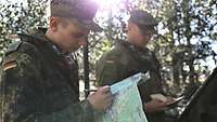 Zwei Soldaten im Wald machen sich Notizen und blicken auf eine Karte.