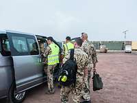 Vier Soldaten steigen in einen grauen Kleinbus. Im Hintergrund erkennt man Container im Camp Sonic.