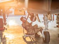 Ein Soldat sitzt unter dem Eurofighter auf einem Stuhl und schaut mit einer Taschenlampe in eine geöffnete Klappe am Rumpf.