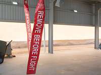 Zwei große rote Anhänger sind zu sehen. Auf ihnen steht „Remove before Flight“. Im Hintergrund sieht man den Shelterbereich.