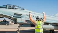 Ein Soldat steht neben einem Eurofighter und gibt dem Piloten im Cockpit Handzeichen. Seine beiden Arme zeigen nach oben.