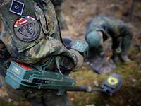 Ein Soldat sucht mit einer großen Handsonde die Bodenoberfläche ab.