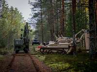Drei spezielle militärische Räumfahrzeuge hintereinander auf einem Waldweg.