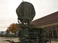 Common Roof SatCom Anlage Eine Satellitenanlage der Bundeswehr steht mit aufgeklapptem Spiegel auf einem Platz vor eine Halle.