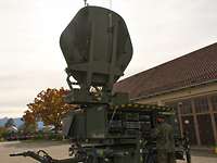 Eine Satellitenanlage der Bundeswehr steht mit aufgeklapptem Spiegel auf einem Platz vor eine Halle.