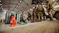 Mehrere Soldaten stehen an einem Fahrzeug und prüfen auf dem Boden stehendes Material