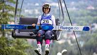 Eine Skispringerin sitzt in der Seilbahn und hält ihre Skier auf dem Schoß.