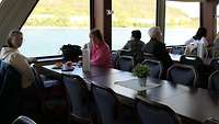 Mehrere Personen sitzen in einem Schiff und schauen auf den Rhein. 