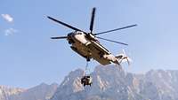 Ein Transporthubschrauber CH-53 transportiert während des Flugs einen Geländewagen Wolf an Seilen.