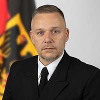 Ein Mann in Uniform vor einer Deutschlandflagge.