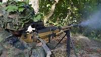 In einem Kampfstand stehend, schießt ein Soldat mit einem Maschinengewehr.