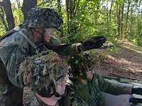 Ein Soldat kniet hinter zwei anderen, erklärt ihnen etwas und zeigt mit der Hand in eine Richtung.