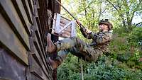 Ein Soldat läuft, die Füße an die Wand gepresst, mit einem Seil in den Händen eine Wand hoch.