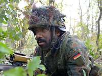 Ein Soldat liegt hinter einem Maschinengewehr MG5 im Wald in Stellung und beobachtet.