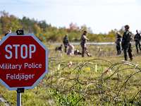Im Vordergrund ein Schild „STOP Military Police Feldjäger“ und im Hintergrund Soldatinnen und Soldaten auf einer Wiese.