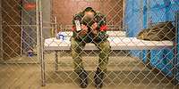 Eine militärisch gekleidete Person sitzt eingesperrt in einem Raum