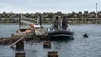 Ein Taucher ragt aus dem Wasser und spricht mit Soldaten auf einem Schlauchboot.