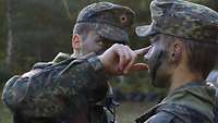 Ein Soldat färbt einem anderen Soldaten das Gesicht mit Schminke grün und schwarz ein