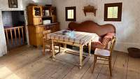 Eine Bauernstube mit Holzfußboden, Küchenschrank und Sofa. 