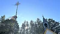 Ein Kirchweihbaum ragt in den blauen Himmel davor ist eine eine Kapelle.