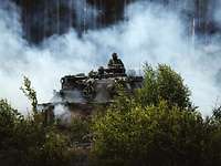 Ein Panzer befindet sich in einem Wald voller Qualm, während zwei Soldaten aus dem Ausguck schauen. 