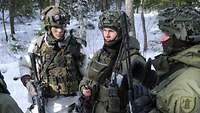 Ein deutscher Soldat steht neben zwei litauischen Soldaten im Schnee, sie unterhalten sich.
