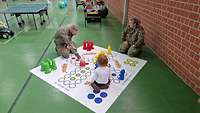 Mann, Frau und Kind sitzen auf einem großen Spieltuch auf dem Boden