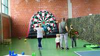 Ein Mann und 4 Kinder in einer Halle stehen vor einem Fussball-Dart