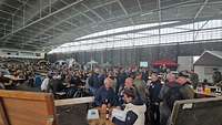 Viele Menschen in einer großen Halle, zum Teil an Tischen sitzend