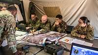 Mehrere Soldaten aus unterschiedlichen Nationen sitzen an einem Tisch und werten eine Karte aus.
