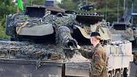 Ein Soldat steht vor der Kanonenmündung eines Kampfpanzers und hält eine grüne Stange.