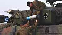 Zwei Soldaten neben einem Panzer reichen Munition mit blauer Spitze einem dritten Soldaten nach oben