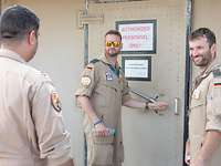 Ein Soldat im Fliegeranzug öffnet eine schwere Stahltür. Davor stehen zwei weitere Piloten.