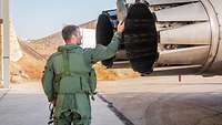 Ein Pilot im Flugdienstanzug steht hinter einem Triebwerk. Die rechte Hand fasst an das Flugzeugheck.