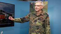 Ein Soldat steht mit halb gehobenem rechtem Arm während eines Interviews vor einer blauen Wand.