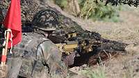 Ein Soldat liegt auf einer Wiese und hat ein Gewehr in der Hand