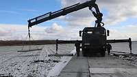 Ein Fahrzeug mit einem Kran setzt große Betonplatten ab.