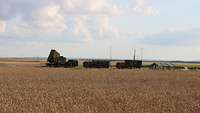 In einem Kornfeld stehen drei LKWs mit einem Radar, einem Generator und einer Feuerleitkabine.