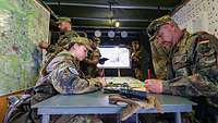 Mehrere Soldaten arbeiten sitzend und stehend im Gefechtsstand an geografischen Karten.