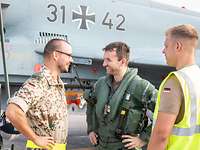 Zwei Soldaten und ein Pilot im Flugdienstanzug stehen vor einem Eurofighter und sprechen miteinander.