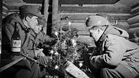 Schwarzweißfoto: Soldaten sitzen in einer Berghütte um einen Weihnachtsbaum herum.