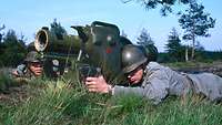Zwei Soldaten liegen auf einer Wiese hinter einer großen Panzerabwehrwaffe.