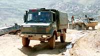 Schwere Lkws fahren einen schmalen Bergpfad hinauf.