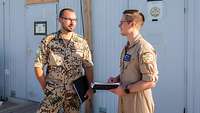 Ein Soldat in Uniform steht neben einem Zivilist in Fliegerkombi vor Bürocontainern.